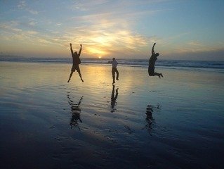 Three people jumping for joy on a beach with a sunset in the background