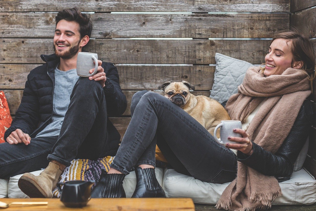 5 Simple Ways to Invest In Your Health This Winter feature image showing a man and a woman sitting laughing. A pug sits between them and the woman holds a mug