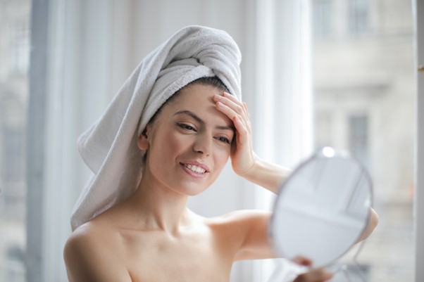 Lady with a towel on her head looking in a hand held mirror