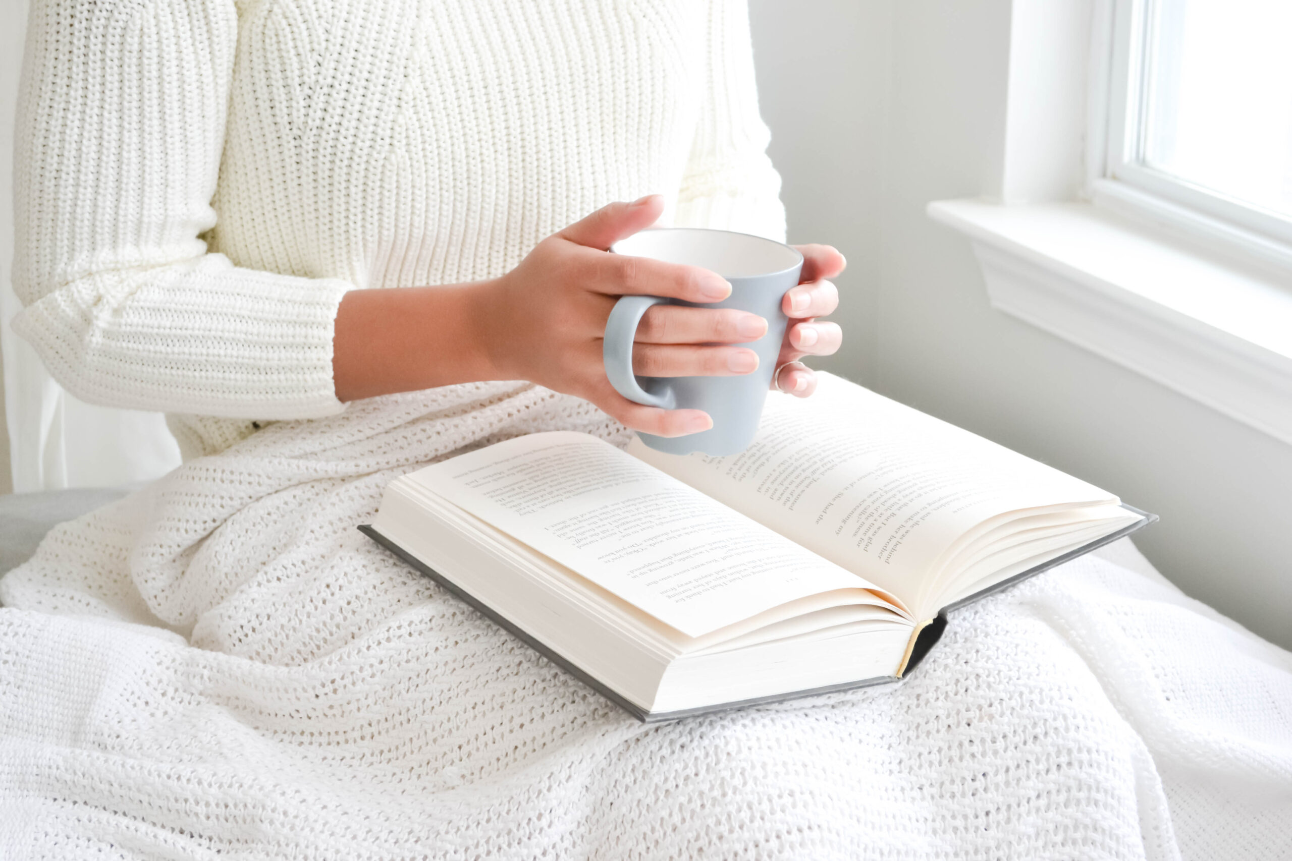 A woman's hands holding a mug over an open book